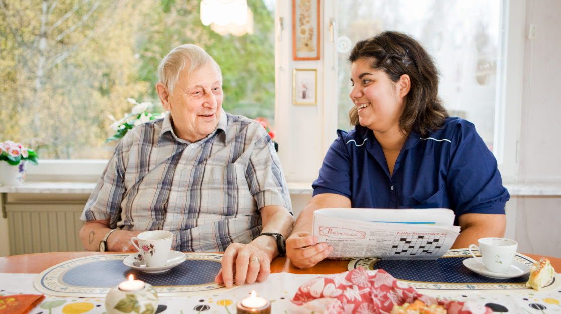 En äldre man och en kvinnlig vårdpersonal pratar vid ett köksbord